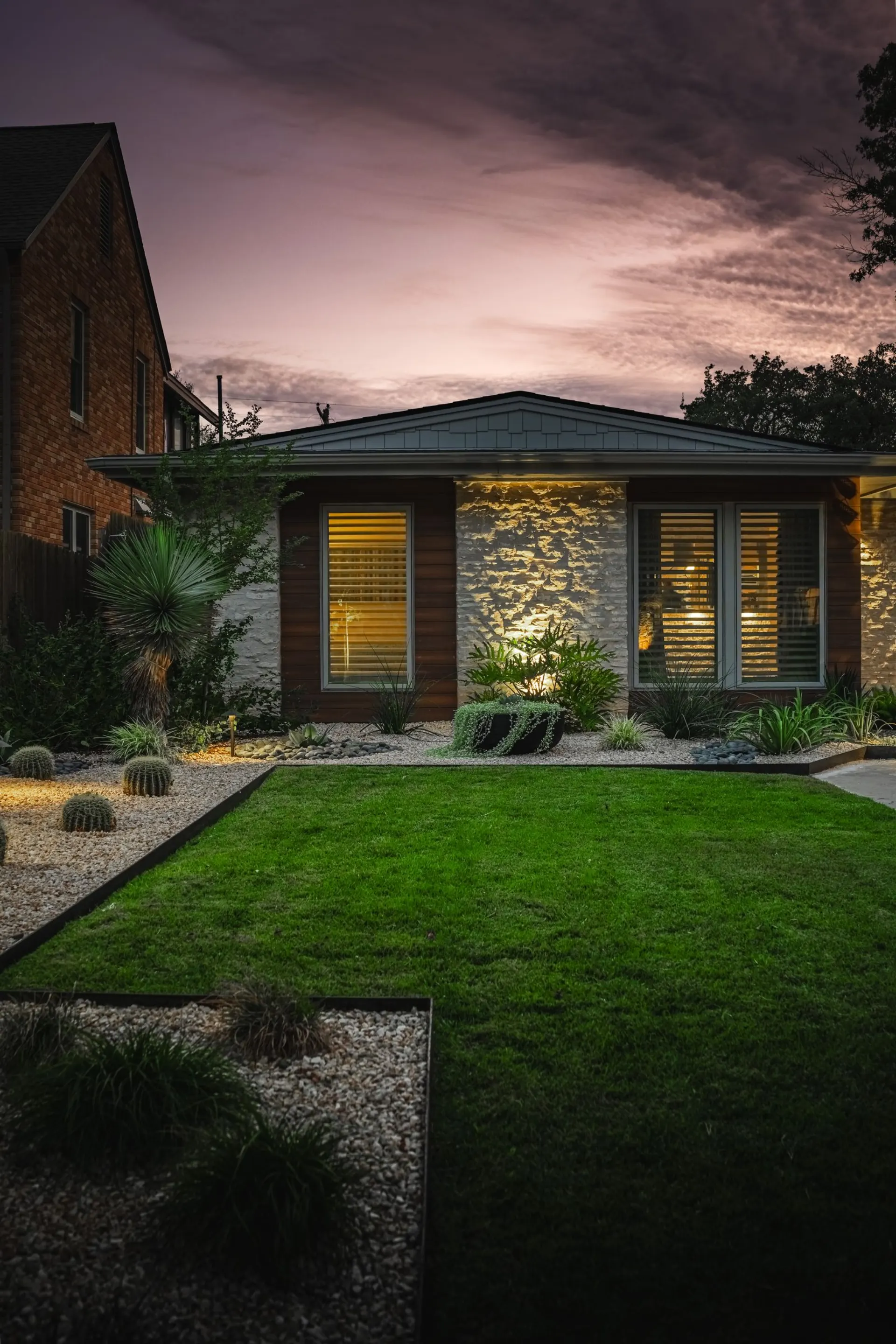 Stone and wood home with gravel beds, cactus and path lighting at dusk