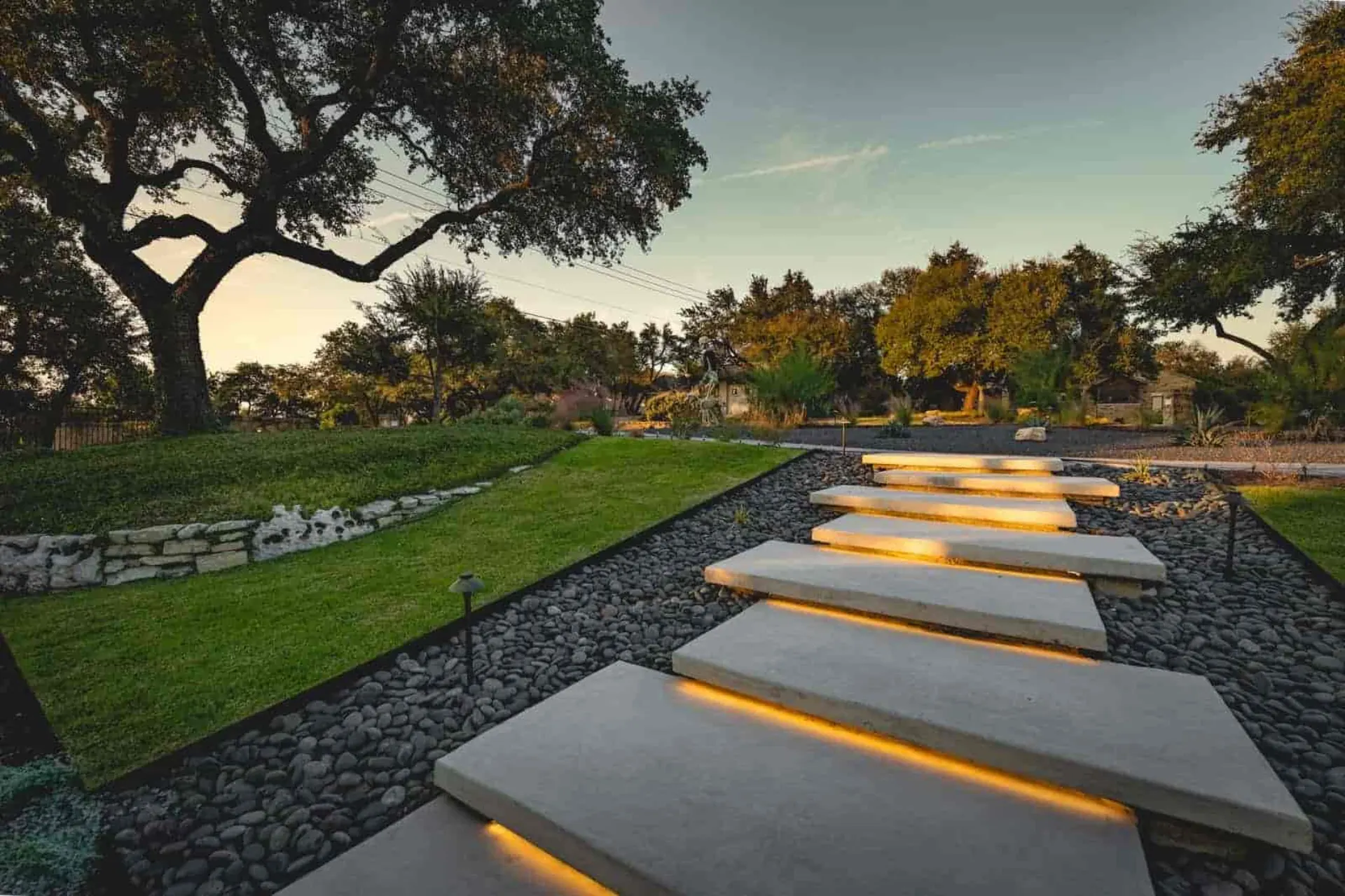 Floating concrete steps with under-lighting through black pebbles and lawn